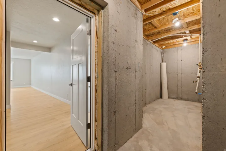 Unfinished concrete walls and flooring, exposed wood ceiling joists, and visible utility lines provide a foundational space