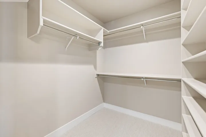 Walk-in closet featuring white shelving, multiple hanging rods, and built-in storage cubbies