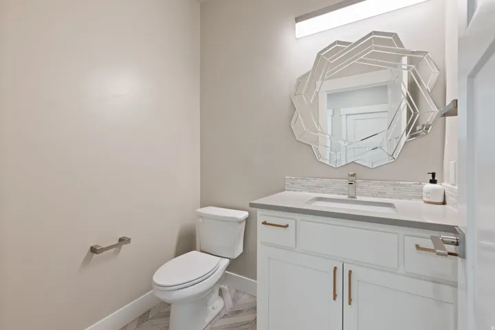 White vanity with a neutral countertop, undermount sink, and tiled backsplash