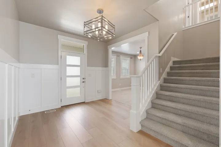 Light wood-finish flooring, white wainscoting, and a carpeted staircase with white railings