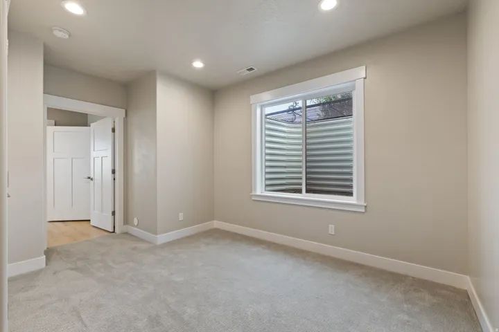 Recessed lighting, light gray carpet, window with white trim, white paneled door, and neutral wall paint