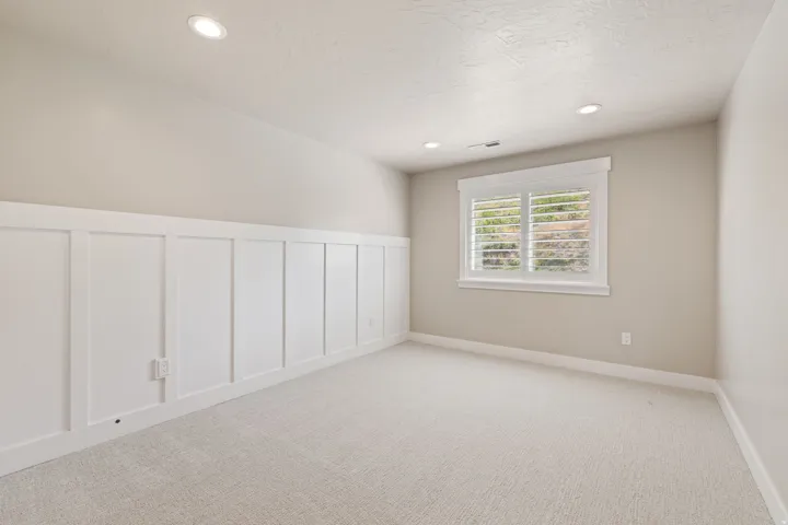 Recessed lighting, light-toned carpeting, window with plantation shutters, white board and batten wall paneling, painted drywall