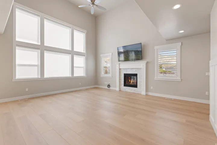 Vaulted ceiling with a ceiling fan, wall of tall windows, wood-finish flooring, and a fireplace with a white mantel and tile surround