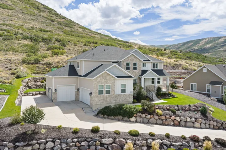 Stone and siding exterior with multiple gables, three attached garage bays, a covered front entry, and sloped landscaping
