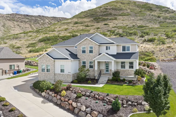 Stone and siding exterior with a covered porch, established landscaping, and an extended paved driveway