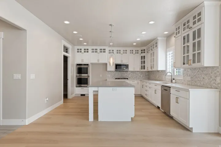 Expansive kitchen featuring white cabinetry, a large central island, stainless steel appliances, a tile backsplash, and wood-finish flooring