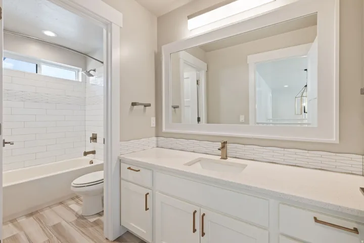 White vanity with integrated sink, quartz countertop, and horizontal tile backsplash