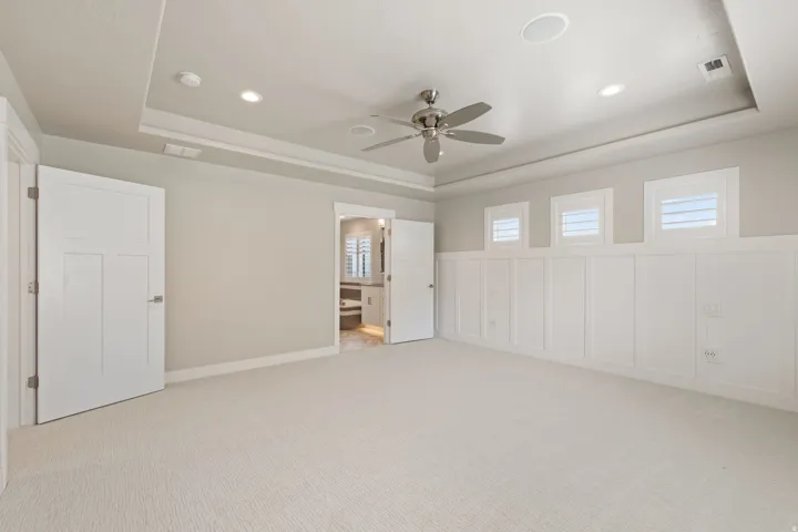 Tray ceiling, recessed lighting, ceiling fan, white board and batten wall paneling, and white plantation shutters