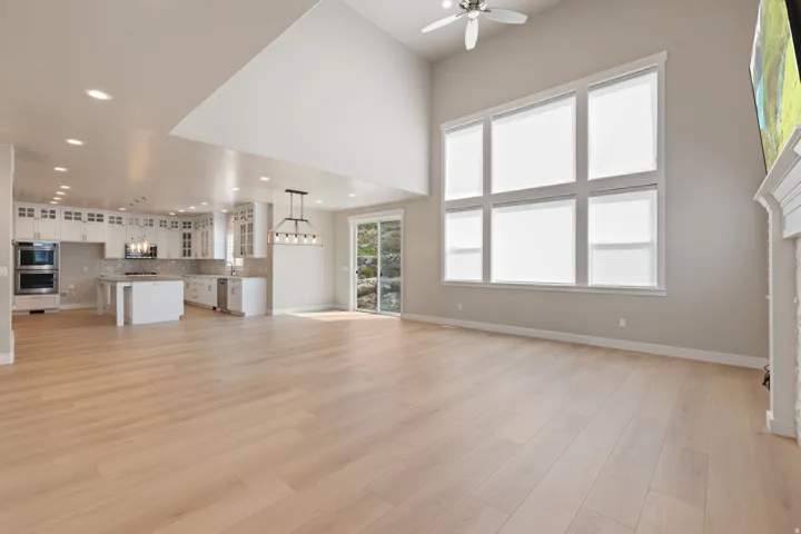 Vaulted ceilings, wood-finish flooring, white cabinetry, built-in double ovens, and a fireplace with a mantel