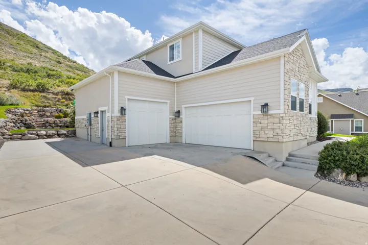 Two-story residence featuring light-toned siding, stacked stone accents, dual garage doors, and exterior lighting fixtures