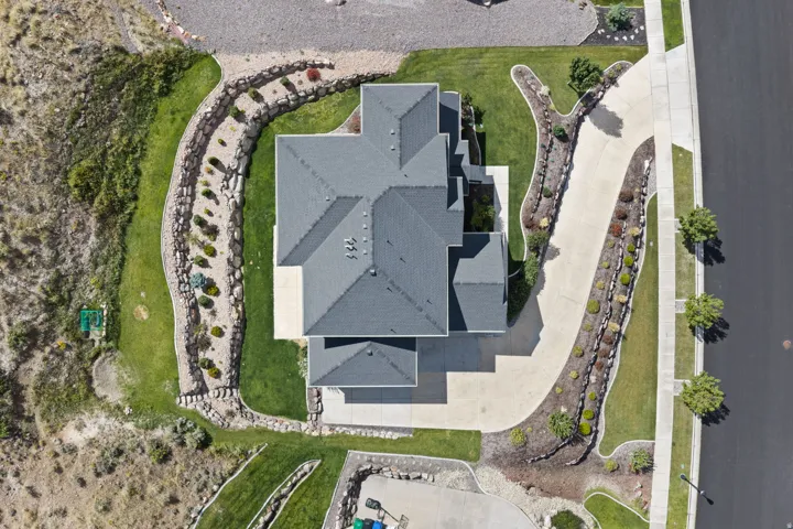 Asphalt shingle roofing, paved driveway, landscaped yard with decorative plantings, and stone retaining walls