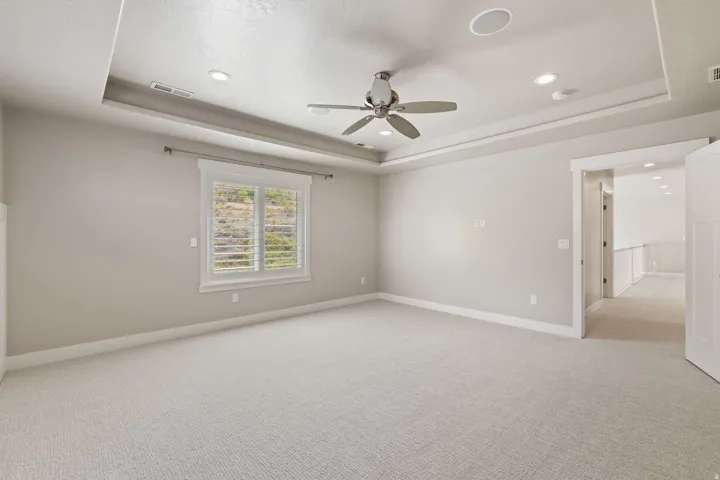 Spacious room featuring tray ceiling, recessed lighting, ceiling fan, carpeting, and window with exterior scenery