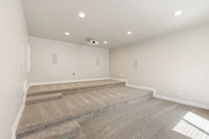 Tiered entertainment room with recessed lighting, wall-mounted speakers, and a ceiling-mounted projector