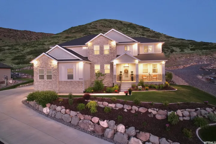 Stone and siding exterior with a covered front porch, concrete driveway, and landscaped rock retaining walls