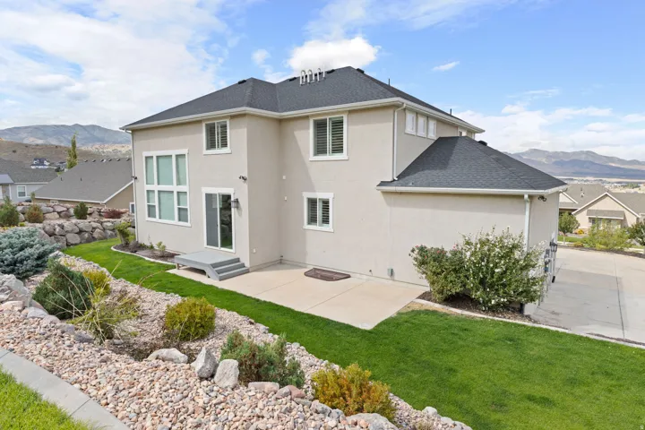 Stucco exterior with a dark shingle roof, a concrete patio, and a rock landscaping feature