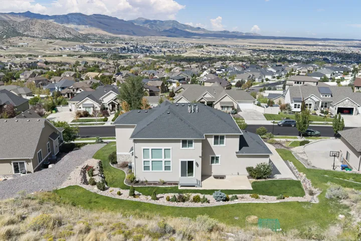 Spacious property featuring a stucco exterior, dark shingle roof, landscaped grounds, and a paved patio area