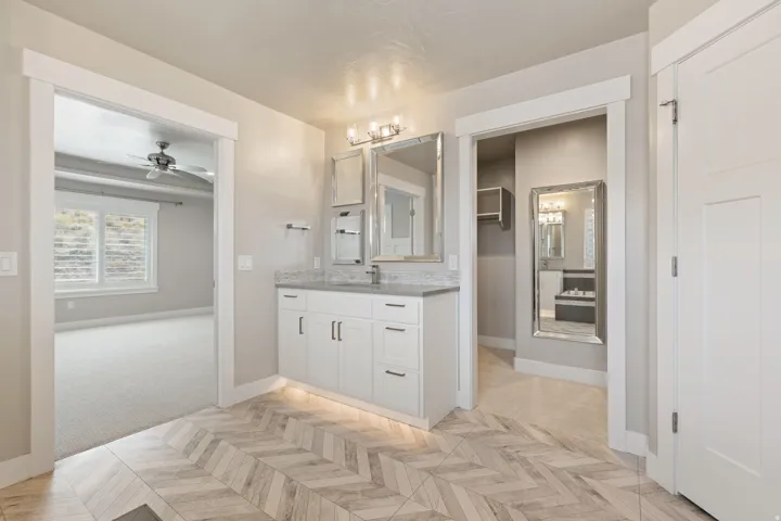 Herringbone wood-finish flooring, white shaker cabinetry, stone countertop, dual vanity mirrors, and recessed lighting