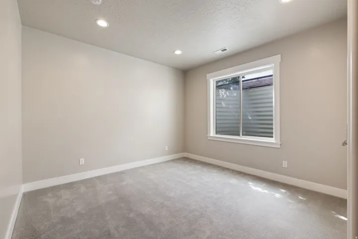 Recessed lighting, neutral wall tones, white trim, gray carpeting, and a single window with a white frame