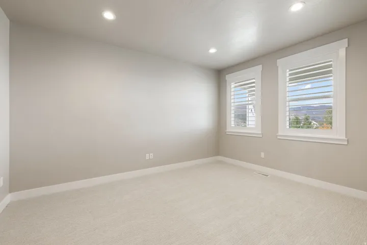 Recessed lighting, light-colored carpeting, two windows with white plantation shutters, and crisp white trim
