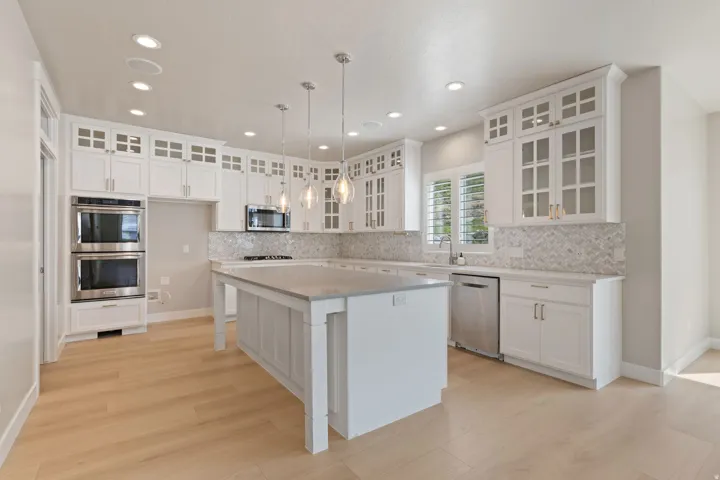 Spacious kitchen featuring white cabinetry, light wood-finish flooring, a large center island, stainless steel double wall ovens, and a mosaic tile backsplash