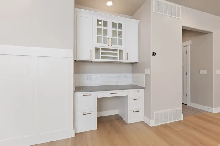 Built-in desk area featuring white cabinetry, a light-toned countertop, and a subway tile backsplash