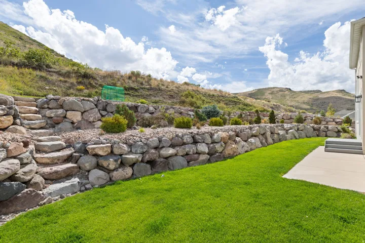 Manicured lawn, stone retaining walls, rock steps, mature landscaping, and concrete patio