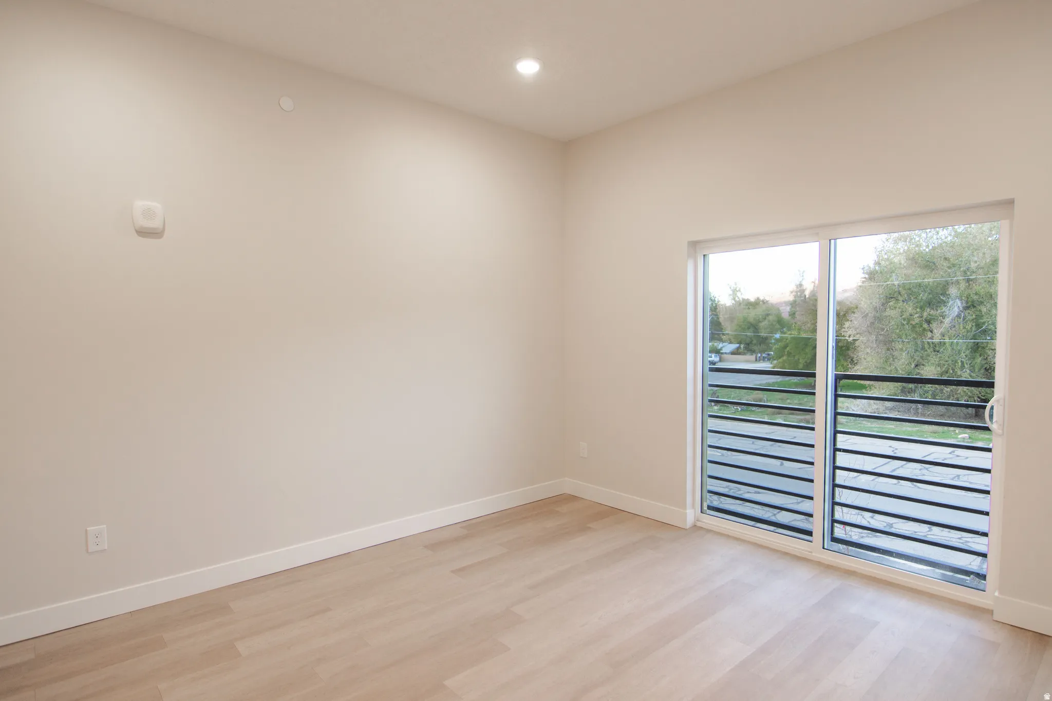 Recessed ceiling lighting, light wood-finish flooring, sliding glass door, and a black metal balcony railing