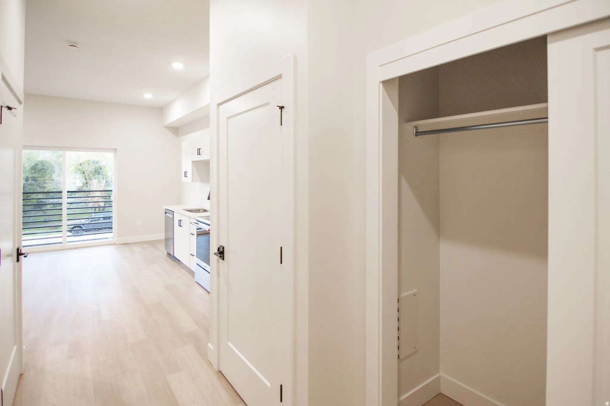 Recessed lighting illuminates the space, featuring wood-finish flooring and a kitchen with white cabinetry