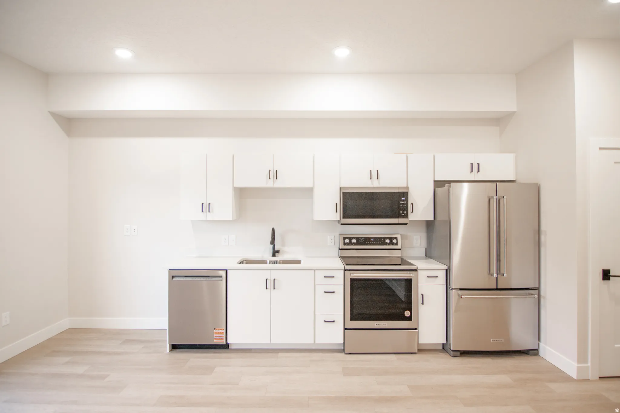 White kitchen cabinetry with stainless steel appliances, including a French door refrigerator, range, microwave, and dishwasher