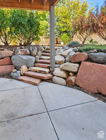 Outdoor space featuring a concrete patio, natural stone tiered steps, and terraced boulder retaining walls accented by mature trees and greenery