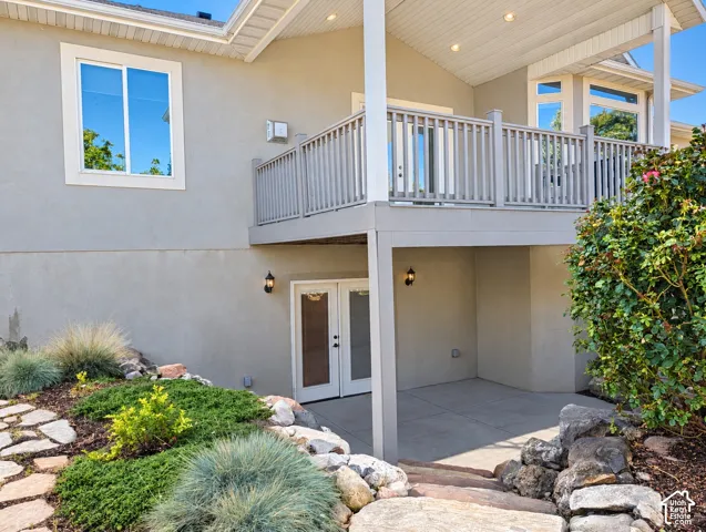 Elevated deck with vertical balusters, concrete patio, double-door entrance, and rock-lined landscaping