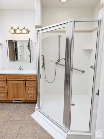Corner shower enclosure with metal-trimmed glass doors, light wood cabinetry, multi-drawer vanity, quartz-surfacing countertop, and tri-light fixture