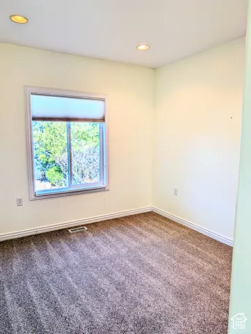 Interior room featuring neutral-toned carpeting, recessed ceiling lighting, and a single-pane window with a light-filtering shade