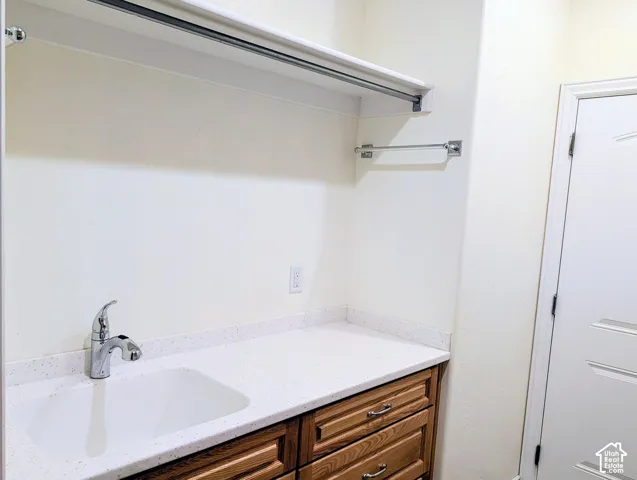 Solid surface countertop featuring an integrated sink with a polished chrome faucet, wooden cabinetry, and overhead shelving with a mounted hanging rod