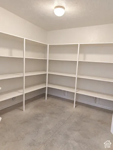 Storage space featuring wrap-around white tiered shelving and concrete flooring, illuminated by a ceiling-mounted light fixture