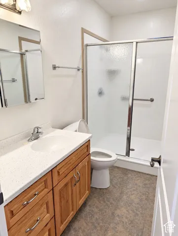 Bathroom featuring a vanity with wood cabinetry and a stone-composite countertop, integrated sink, shower stall with a glass sliding enclosure, and textured flooring