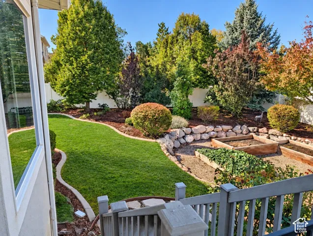 Backyard featuring a tiered stone retaining wall, manicured lawn with concrete edging, built-in wooden garden beds, and mature landscaping