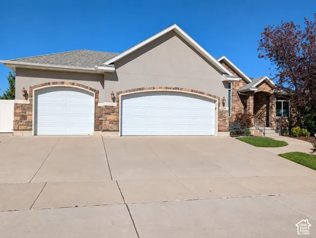 Stucco and stone veneer exterior featuring an attached three-car garage with arched entryways, asphalt shingle roofing, and a concrete driveway