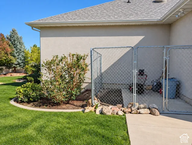 Exterior space featuring stucco siding, a concrete patio, landscaped garden beds with stone edging, and chain-link fencing