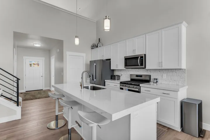 Kitchen featuring a center island with sink, stainless steel appliances, white cabinetry, and a tile backsplash