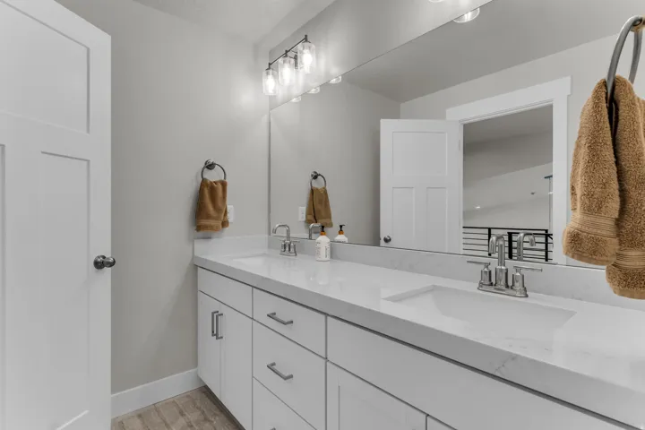 Dual vanity with white cabinetry, integrated sinks, chrome faucets, and a large wall-mounted mirror