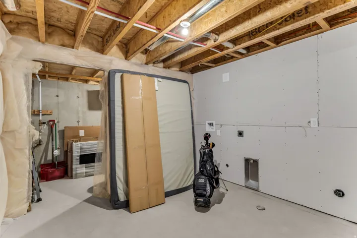 Unfinished basement space featuring exposed joists, concrete foundation walls, partially drywalled sections, and a concrete floor