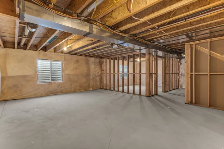 Unfinished lower level with concrete flooring, exposed wood joists, framed interior walls, and an egress window