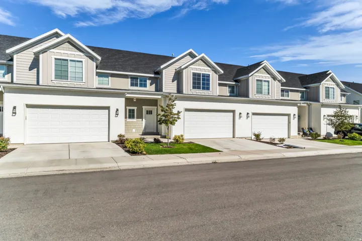 Contemporary townhome exterior featuring light siding, dormer windows, attached garages, and a paved driveway