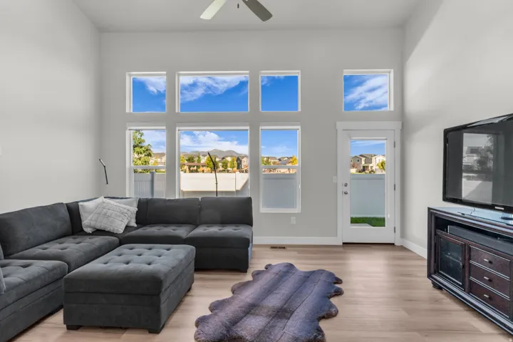 Vaulted ceiling with a ceiling fan, light wood-finish flooring, and multiple transom windows