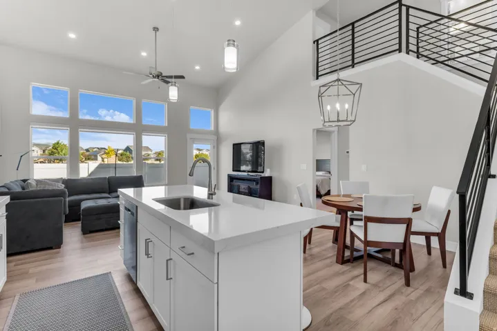 Open-concept living space with vaulted ceilings, a central kitchen island featuring a sink and white cabinetry, expansive windows, and wood-finish flooring