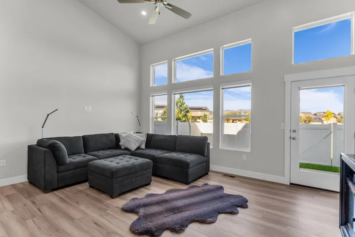 Vaulted ceiling with a ceiling fan, multiple tall windows, light wood-finish flooring, and a white exterior door with glass paneling