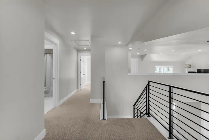 Carpeted hallway with recessed lighting, white trim, and a modern black metal railing