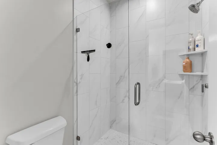 Glass-enclosed shower with white tiled walls, built-in shelving, and a rain shower head
