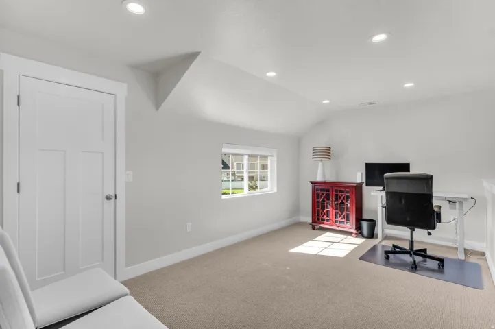 Recessed lighting, sloped ceiling, egress window, white trim, and neutral carpeting